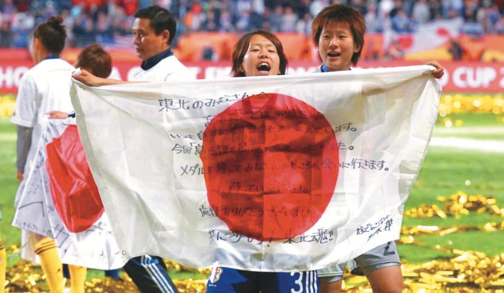 日本隊2011年奪冠後，隊員展示寫有「東北魂」、「我們會帶回獎盃」等集氣口-號的國旗。圖／FIFA